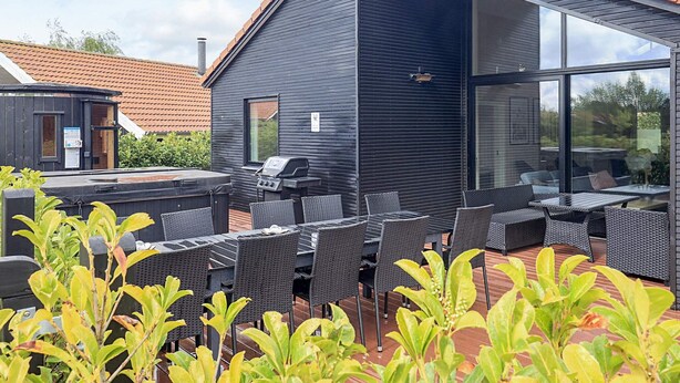 A modern outdoor patio with a grill, wicker furniture, and a view of the surrounding area. - 5 Star Holiday Home in Vaeggerlose (Vaeggerlose)