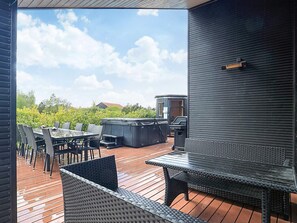 A covered outdoor deck with a table and chairs, a hot tub, and a grill. - 5 Star Holiday Home in Vaeggerlose (Vaeggerlose)