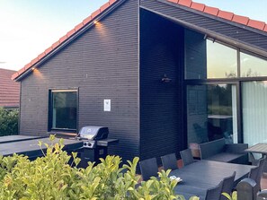 A modern building with a flat roof, a large window, and a barbecue grill. - 5 Star Holiday Home in Vaeggerlose (Vaeggerlose)