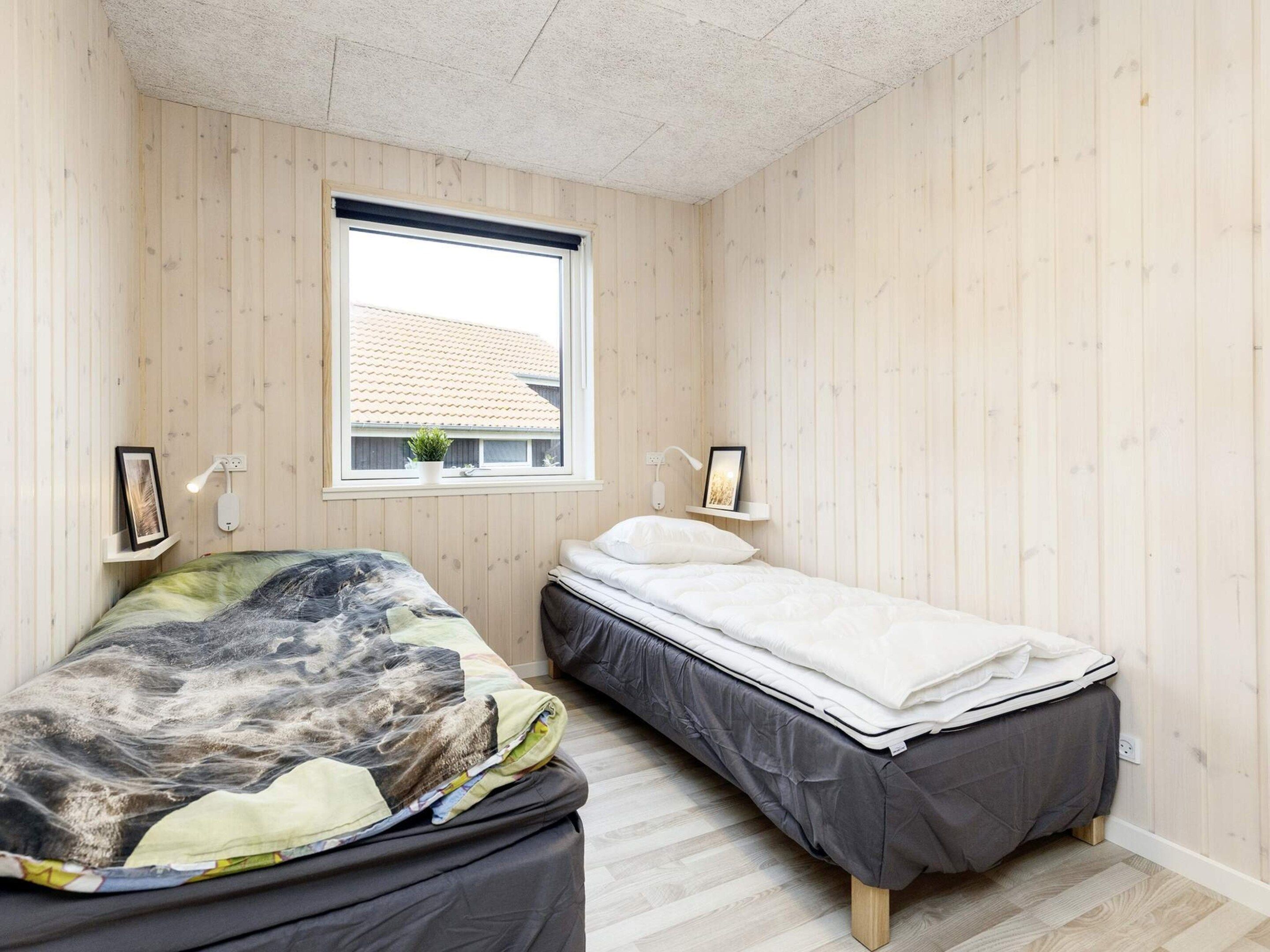 A bedroom with two beds, wooden walls, a window, and bedside lamps.