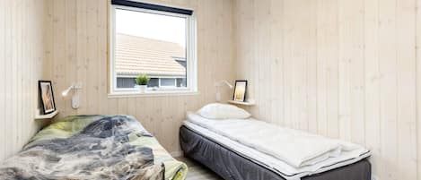 A bedroom with two beds, wooden walls, a window, and bedside lamps.
