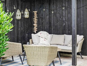 A wicker sofa with cushions against a dark wooden backdrop, surrounded by wicker chairs and a hanging light fixture. - 6 Person Holiday Home in Idestrup (Idestrup)