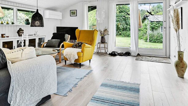 A spacious living room with a yellow armchair, a sofa, and a television. There is a large window with a view of a garden. - 6 Person Holiday Home in Idestrup (Idestrup)