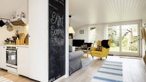A modern kitchen with a chalkboard, a dining area with a yellow chair, and a living room with a sofa and a TV. - 6 Person Holiday Home in Idestrup (Idestrup)