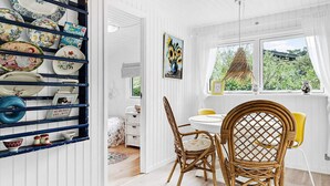 A dining area with wicker chairs and a round table, a shelf with plates, and a window with a view of greenery. - 6 Person Holiday Home in Idestrup (Idestrup)