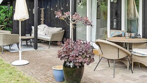 A covered outdoor seating area with wicker furniture, a large potted plant, and string lights. - 6 Person Holiday Home in Idestrup (Idestrup)