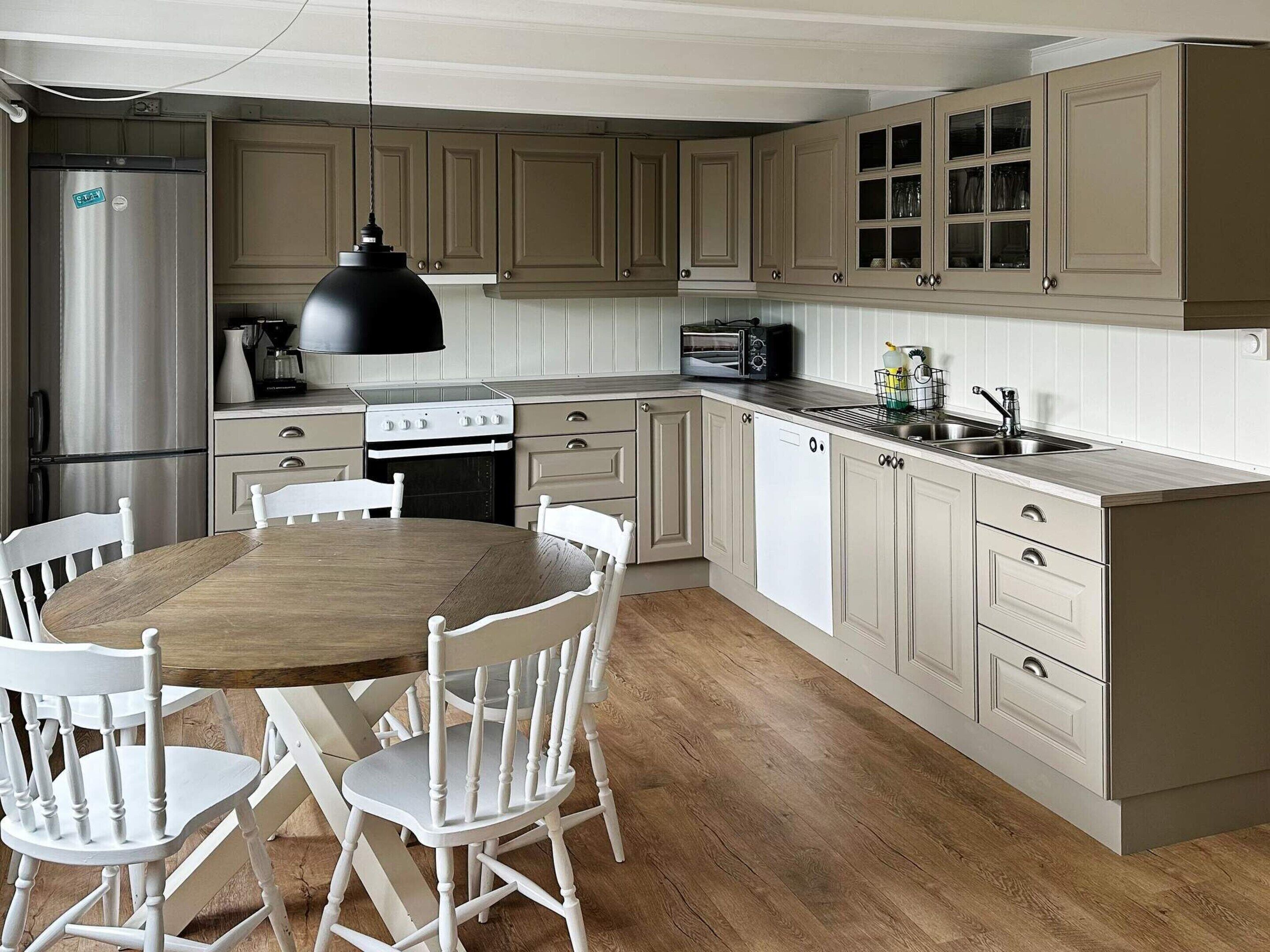 A kitchen with a wooden table and chairs, a stove, a refrigerator, and cabinets.