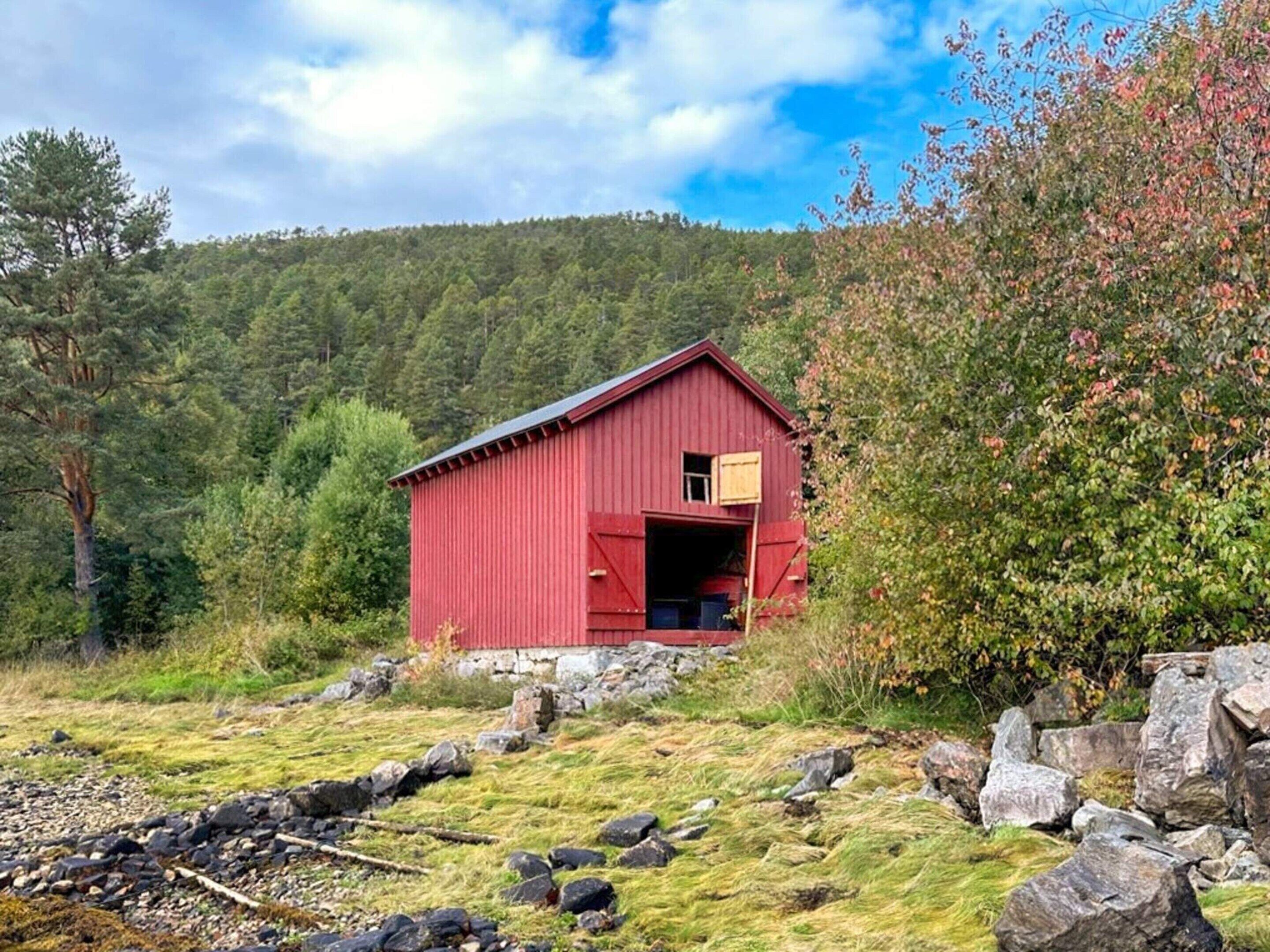 A red barn with a small door and window, surrounded by rocks and greenery.