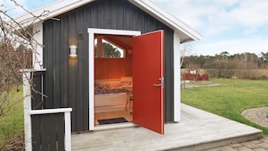 A small, single-room cabin with a red door, a wooden deck, and a view of the surrounding landscape. - 6 Person Holiday Home in Laeso (Læsø)