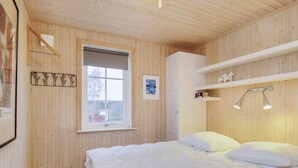 A wooden-paneled room with a bed, a window, a white wardrobe, and a shelf with a lamp. - 6 Person Holiday Home in Laeso (Læsø)