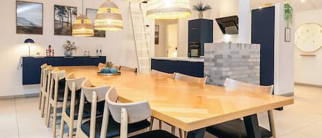 Un comedor moderno con una mesa de madera larga, múltiples sillas y lámparas colgantes.