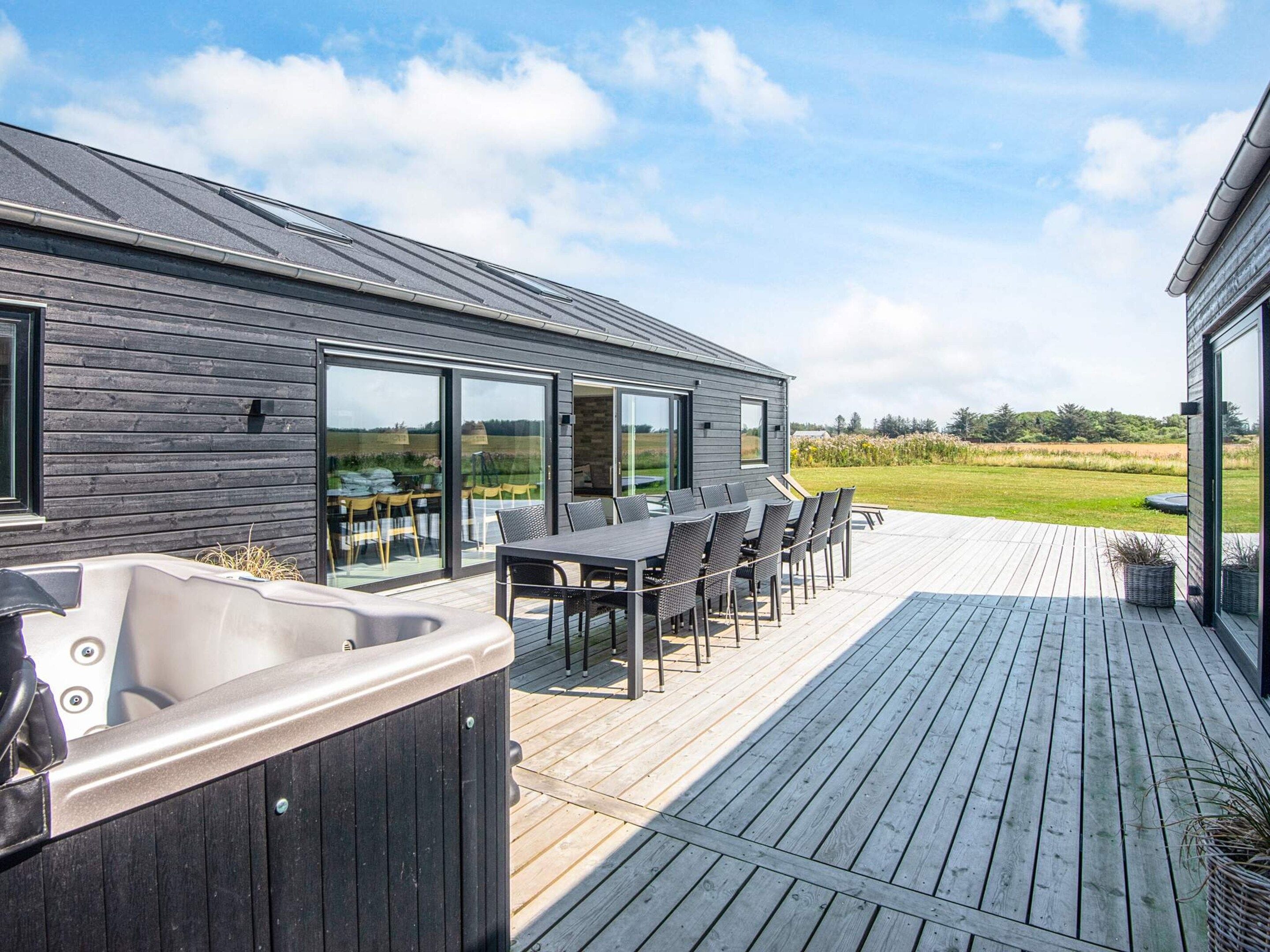 Une terrasse extérieure moderne dotée d’un jacuzzi, d’un espace repas et de grandes portes-fenêtres coulissantes donnant sur un champ verdoyant.