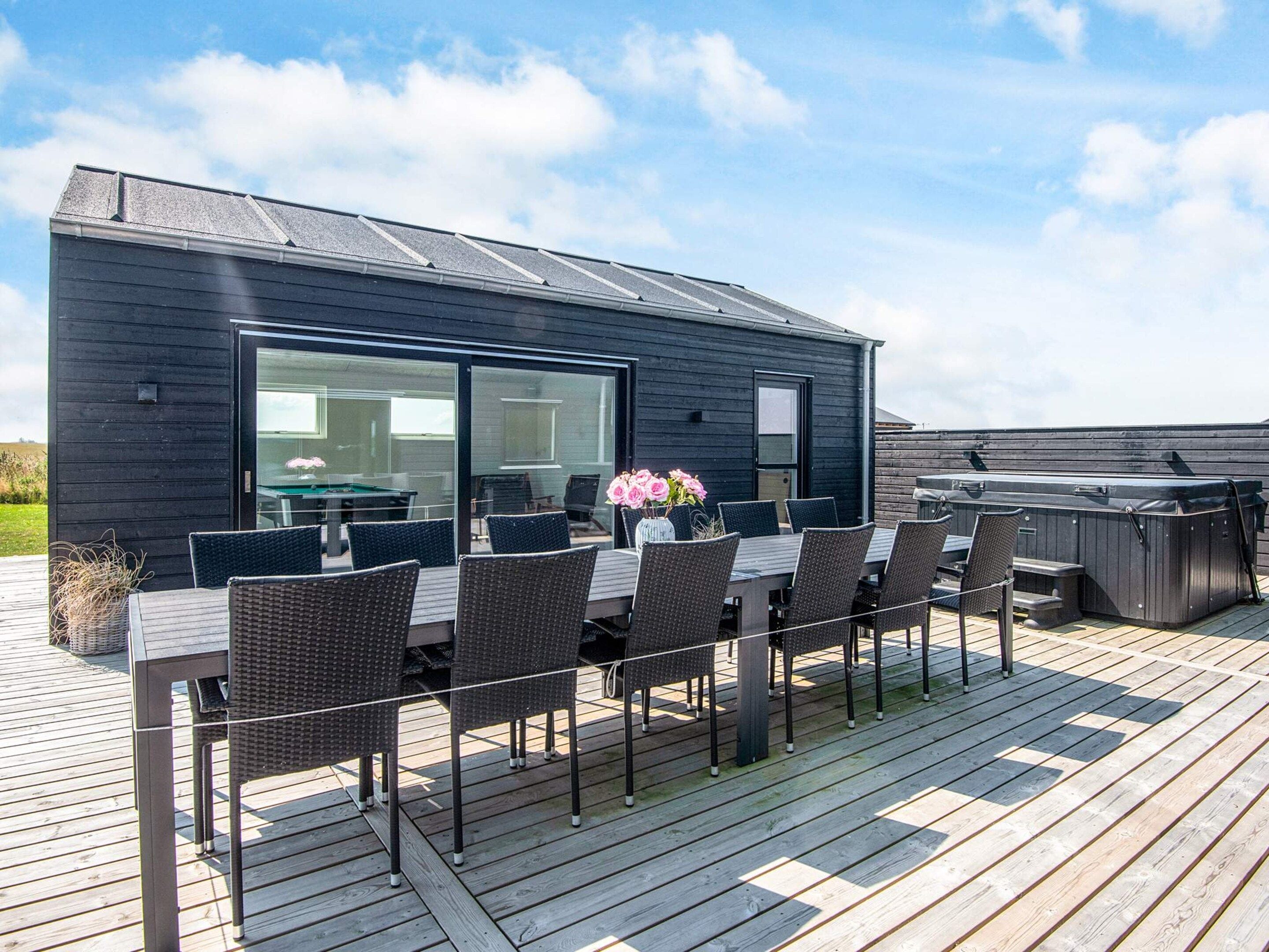 A modern outdoor deck with a dining table and chairs, a hot tub, and a glass-enclosed room.
