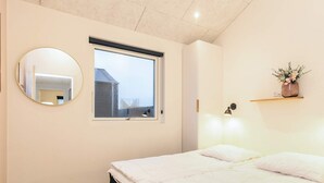 Un dormitorio con cama, un espejo redondo, una ventana y un estante en la pared con un florero.