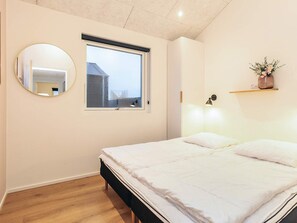 Una camera da letto con un letto, uno specchio rotondo, una finestra e una mensola a parete con un vaso.