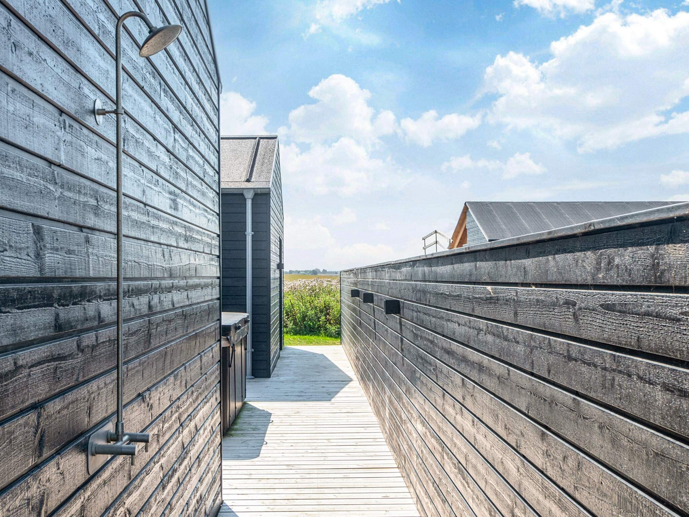 Une terrasse en bois mène à un bâtiment moderne doté d’une rambarde en métal, et le ciel est dégagé.