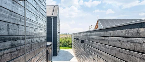 A wooden deck leading to a modern building with a metal railing and a clear sky.