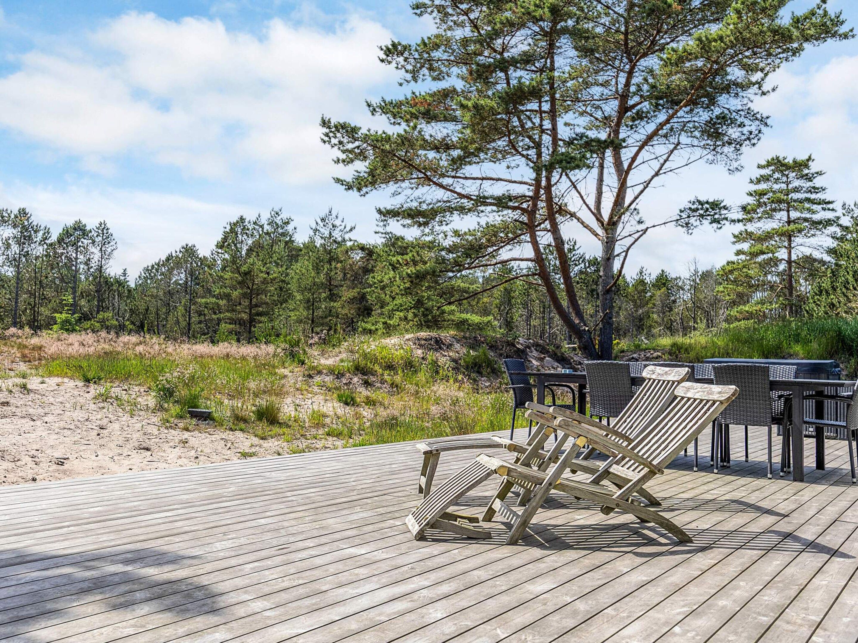 A wooden deck with lounge chairs and a table, surrounded by a forested area.