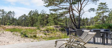 A wooden deck with lounge chairs and a table, surrounded by a forested area.