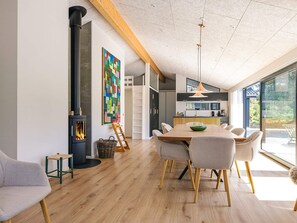 A modern kitchen with a large island, a dining area with a wooden table and chairs, and a fireplace. - 5 Star Holiday Home in Albaek (Aalbaek)