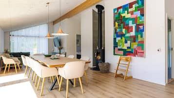 A spacious dining area with a long table and chairs, a fireplace, and a colorful abstract painting on the wall.