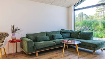 A modern living room with a green sectional sofa, a small red side table, and a round coffee table.