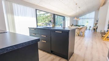 Et moderne køkken med en stor ø, mørke skabe og udsigt til det fri.