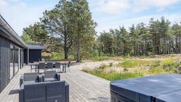 Una terraza con mobiliario exterior, una parrilla cubierta y zona boscosa.