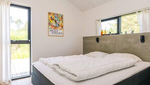 Un dormitorio con cama, ventana con cortinas, lámpara de pared y un cuadro.