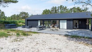 Een modern gebouw met een donkere gevel, grote glasramen en een overdekt terras.