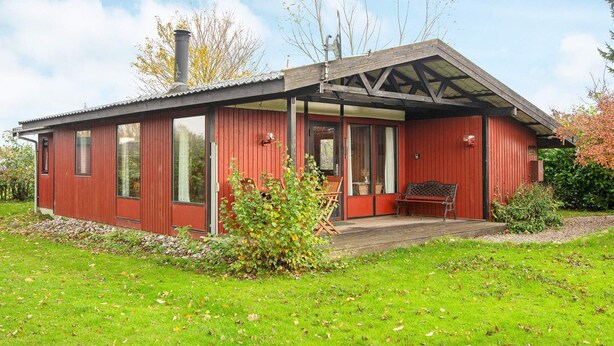A red wooden cabin with a covered porch, large windows, and a chimney. - 6 Person Holiday Home in Sydals (Sydals)