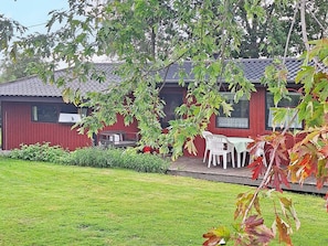 A red building with a tiled roof, a small patio with a table and chairs, and a grassy yard.