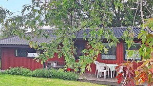 A red building with a tiled roof, a small porch with white plastic chairs, and a grassy yard. - 6 Person Holiday Home in Sydals (Sydals)