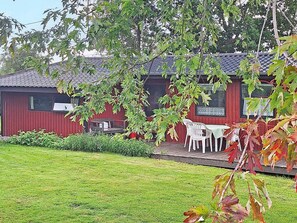 Un bâtiment rouge avec un toit en tuiles, un petit porche avec des chaises en plastique blanches et une cour verdoyante.