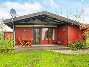 Un bâtiment en bois rouge avec un patio couvert, une antenne parabolique, ainsi qu’une table et des chaises à l’extérieur.