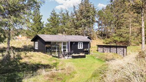 Een chalet met een glazen deuropgang, een terras met buitenmeubilair en een opbergruimte met een stenen muur.