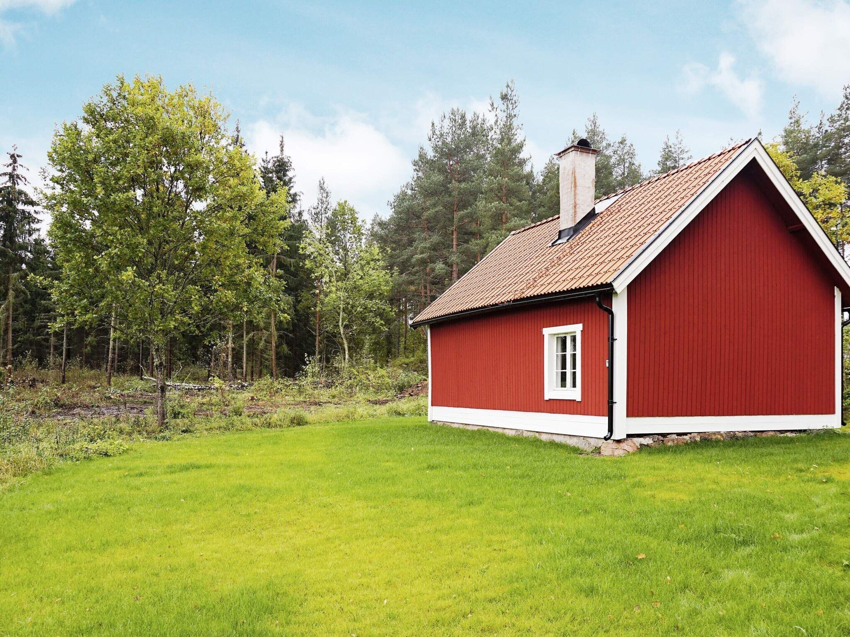 Una casa de madera roja con ventana y chimenea blancos, rodeada de un campo cubierto de hierba y árboles.
