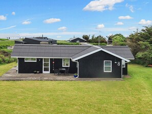 A two-story house with a black exterior and a grey roof, number 8, with a small patio and a door leading to a covered porch. - 6 Person Holiday Home in Lokken (Lokken)