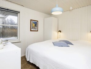 A bedroom with a bed, a bedside table, a framed picture on the wall, and a window with a view of trees. - 6 Person Holiday Home in Lokken (Lokken)