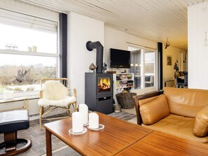 A cozy living room with a fireplace, leather sofa, and a dining area with a table and chairs. - 6 Person Holiday Home in Lokken (Lokken)