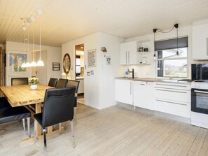 A modern kitchen with white cabinetry, a wooden dining table, and black chairs. - 6 Person Holiday Home in Lokken (Lokken)