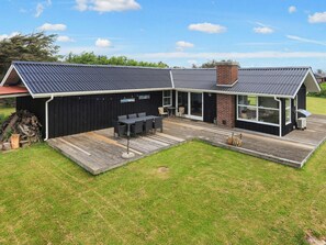 A modern house with a covered patio, a brick fireplace, and a large windowed extension. - 6 Person Holiday Home in Lokken (Lokken)