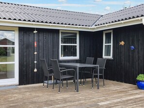 A black building with a tiled roof, a table with chairs, and a blue pot on the deck. - 6 Person Holiday Home in Lokken (Lokken)