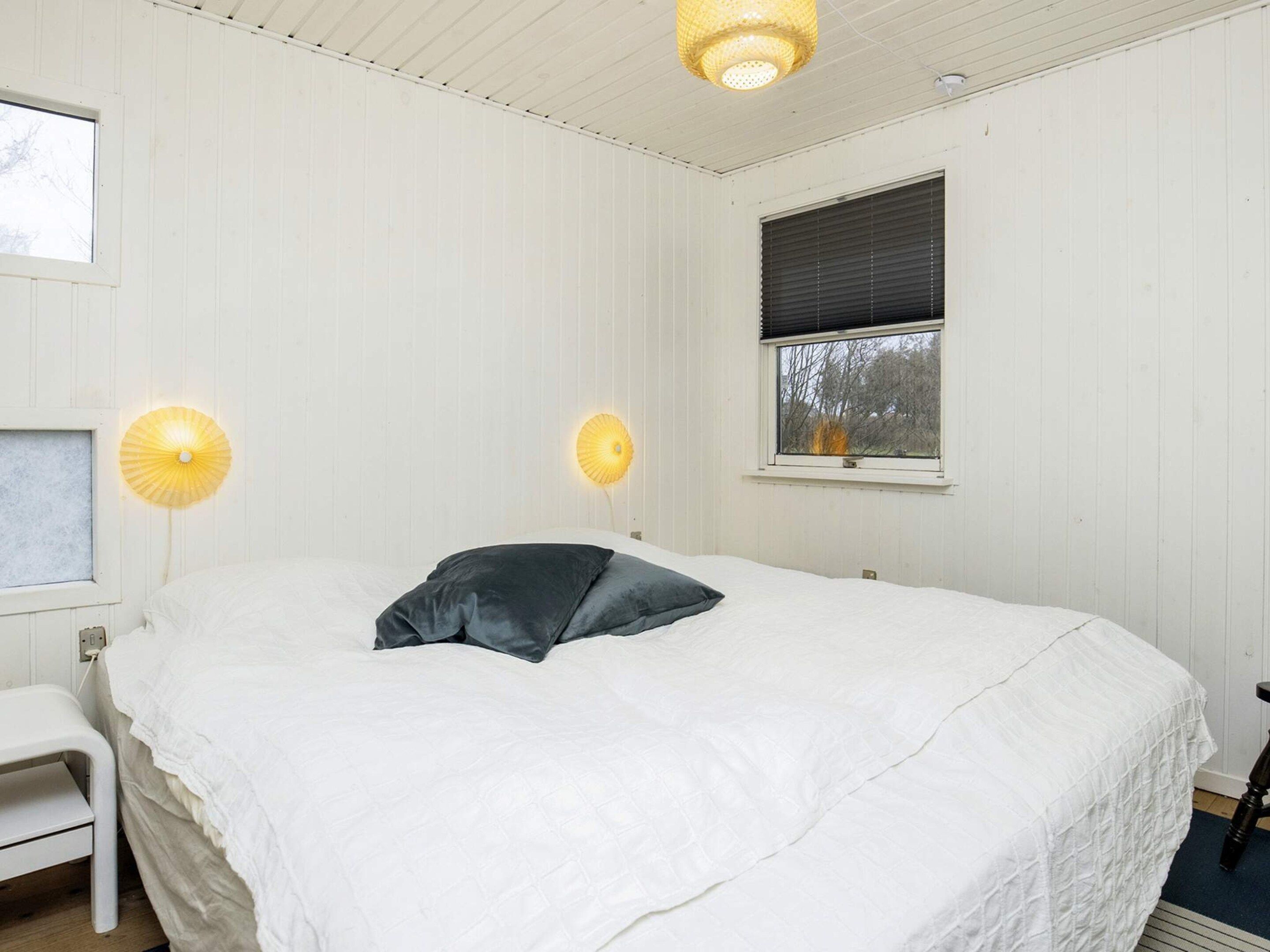 A bedroom with a bed, bedside lamps, a window, and a chair.