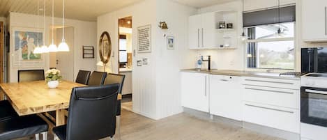 A modern kitchen with white cabinetry, a wooden dining table, and black chairs.
