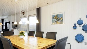 Ein Essbereich mit einem Holztisch, schwarzen Stühlen, Pendelleuchten, einer Blumenvase und einem Bild an der Wand.