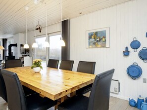 A dining area with a wooden table, black chairs, pendant lights, a vase with flowers, and a painting on the wall. - 6 Person Holiday Home in Lokken (Lokken)