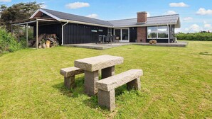 Ein modernes Haus mit einer überdachten Terrasse, einer Steinsitzbank und einem Rasenstück.