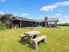 A modern house with a covered patio, a stone bench, and a grassy yard. - 6 Person Holiday Home in Lokken (Lokken)