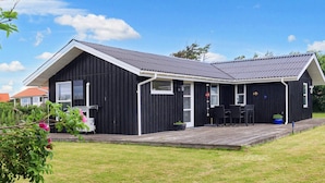 Une maison en bois peinte en noir, avec un toit gris, une véranda dotée d’une table et de chaises, et un petit jardin.